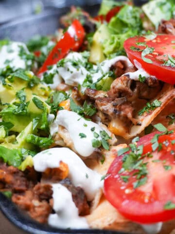 nachos topped with fresh avocado, tomatoes, sour cream and cilantro in a Lodge Cast Iron Skillet.