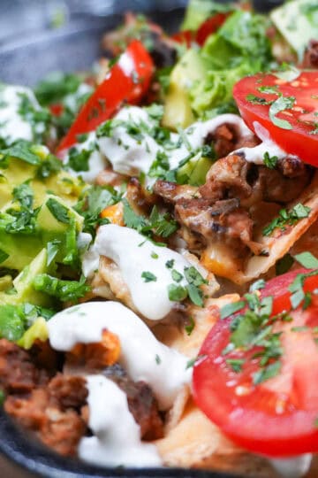 nachos topped with fresh avocado, tomatoes, sour cream and cilantro in a Lodge Cast Iron Skillet.