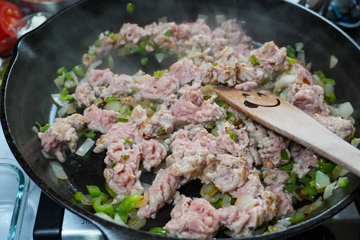 ground turkey added to sauteed onions and bell peppers in a skillet.