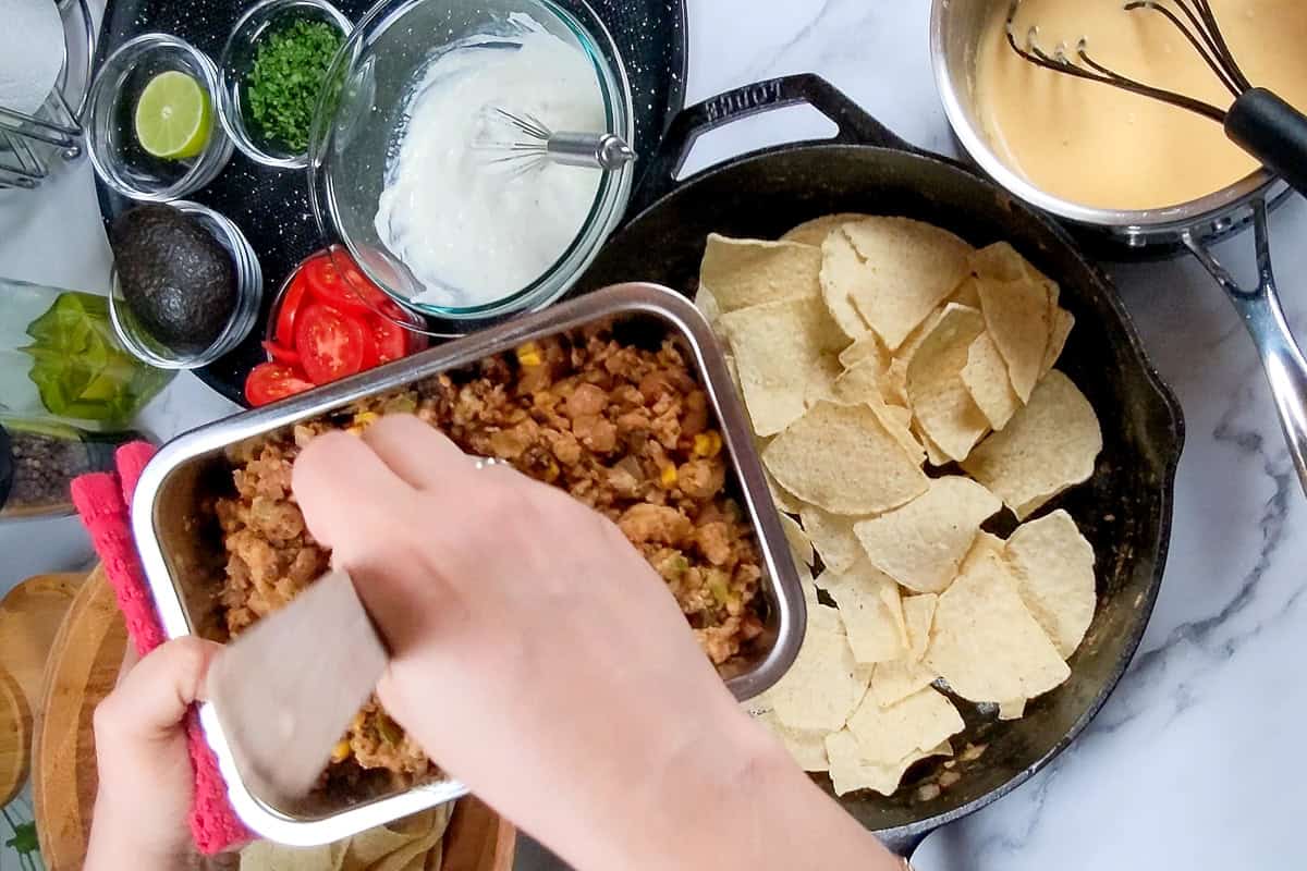 ground turkey mixture being added to a layer of corn tortilla chips in a greased lodge cast iron skillet.