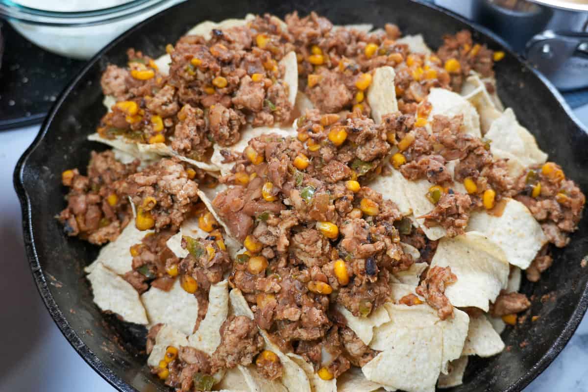 close up of the ground turkey mixture on a layer of corn tortilla chips in a cast iron skillet.