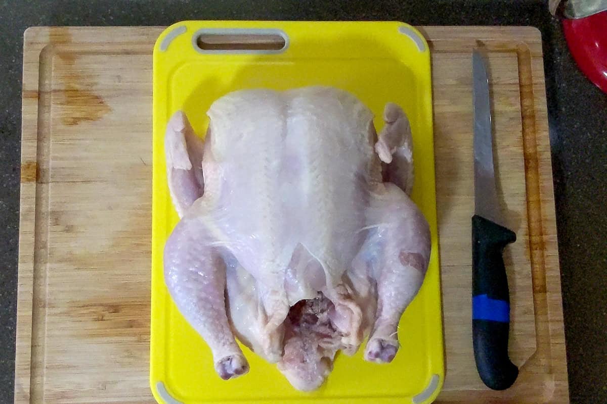 chicken placed on a plastic cutting board for raw poultry with a boning knife next to it.