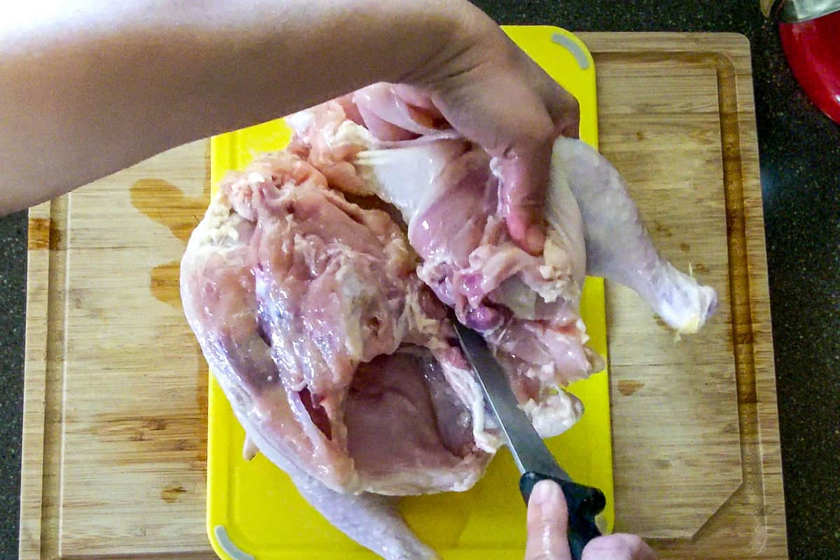 using the knife to completely remove the thigh from the chicken carcass.