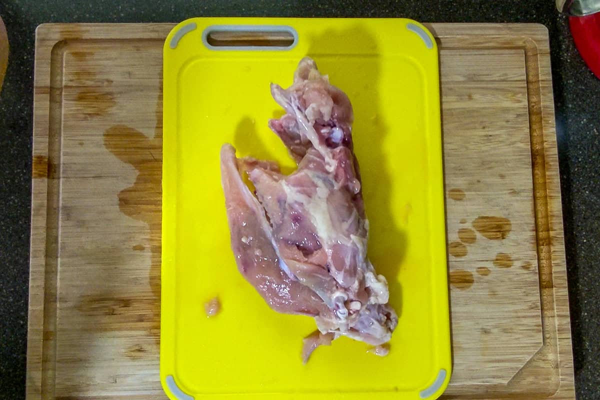 chicken carcass with all the quarters removed on a plastic cutting board.