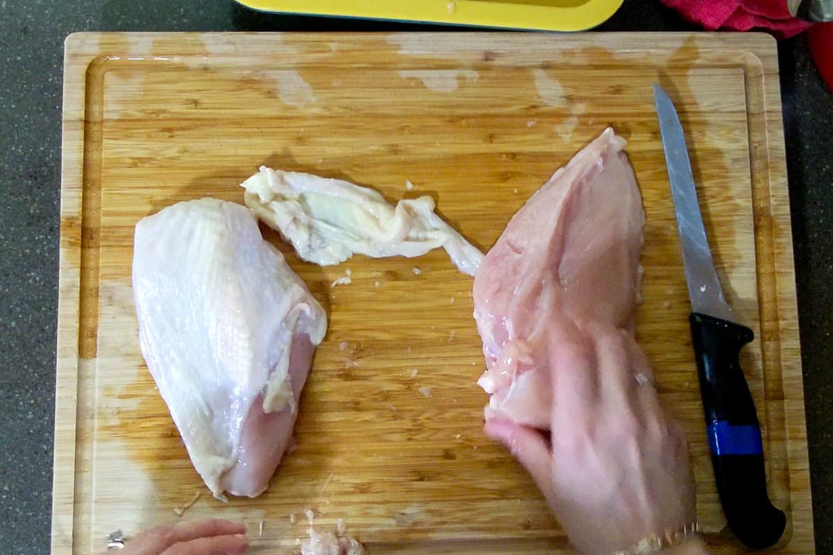 skin on chicken breast and skinless chicken breast next to the chicken skin on the cutting board.