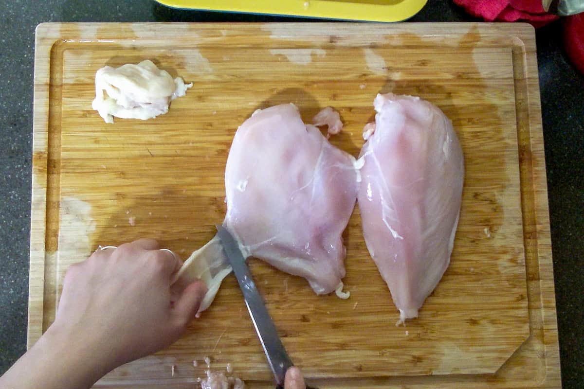 using a knife to remove the chicken skin from the breast.