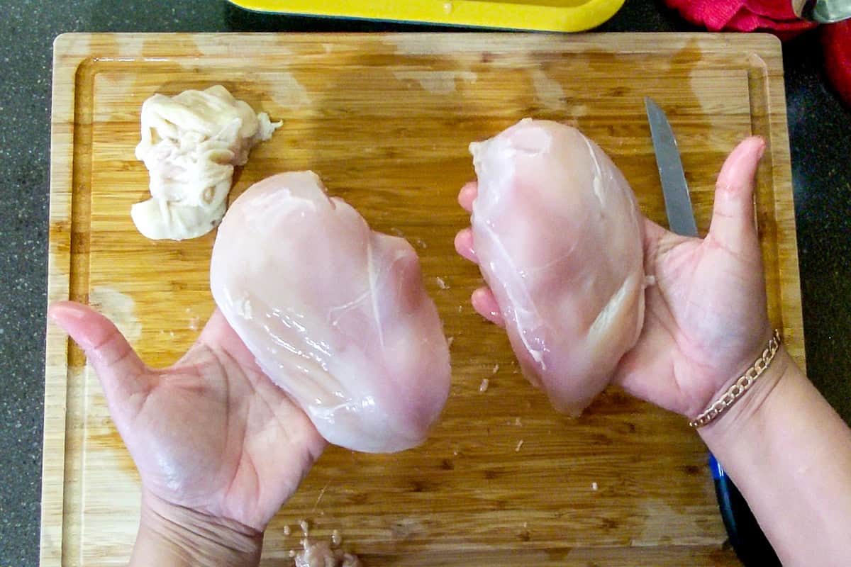 chef showing skinless boneless chicken breast in hands.