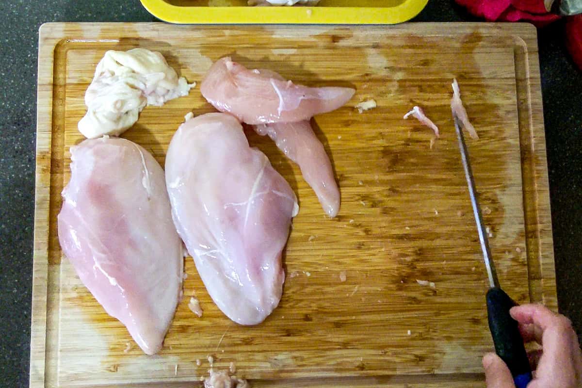 showcasing the skinless chicken breasts next to the skinless tenderloins and the leftover chicken skin on the cutting board.