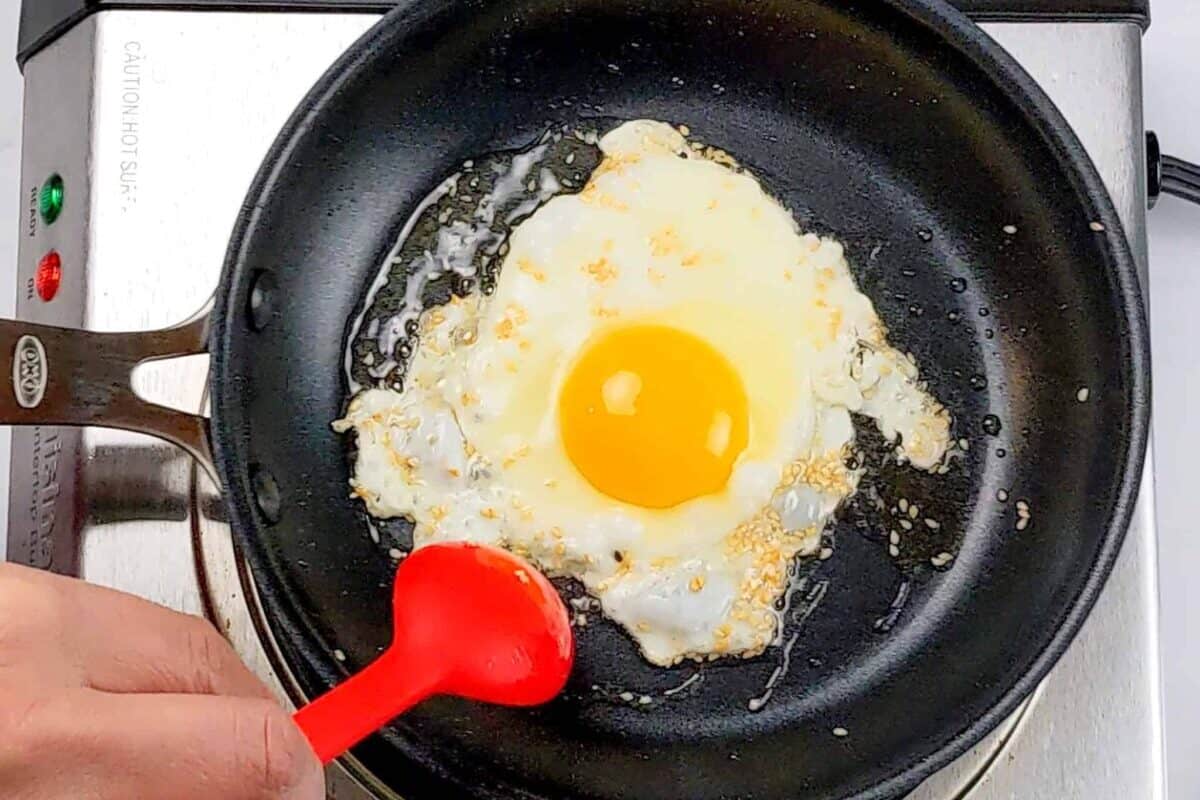 sesame seeds and oil being spooned over the fried sunny side egg with a silicone spoon made by GIR.
