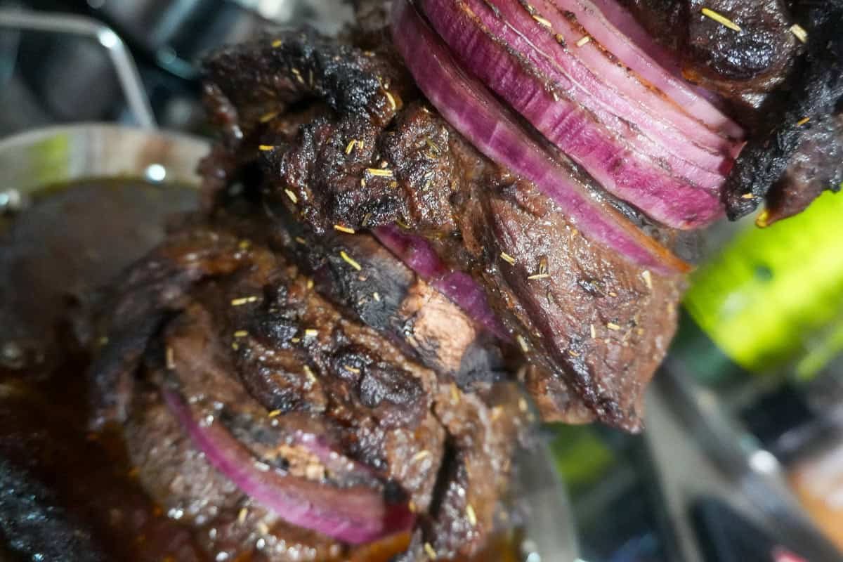 close up of steak shawarma on a vertical skewer with purple onions slices and portobello mushrooms.