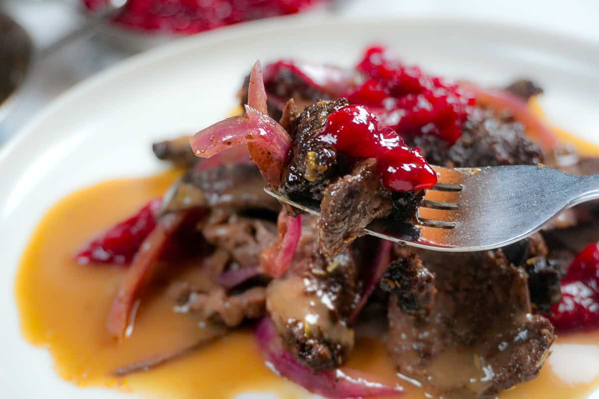 close up of the plate with red onions, steak and cranberry chutney on a fork.