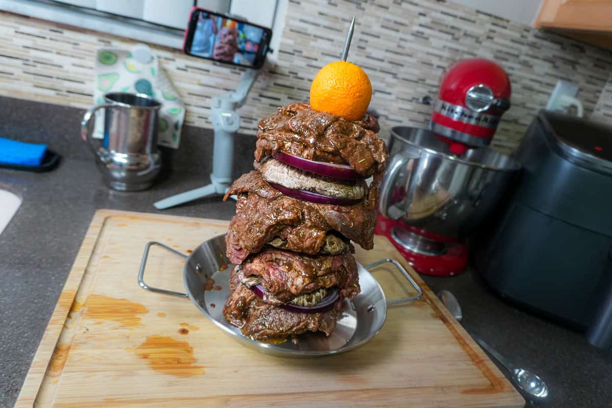 steak, onion and mushroom stacked on the vertivle skewer with an orange on top, ready for the oven.