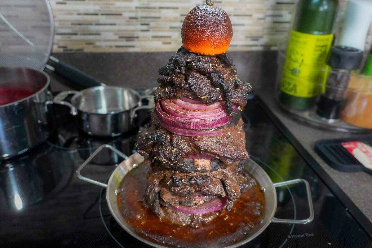 roasted steak shwarma on the vertical skewer with drippings in the pan.