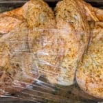 haitian style seasoned spatchcock turkey on a sheet tray covered in plastic wrap.