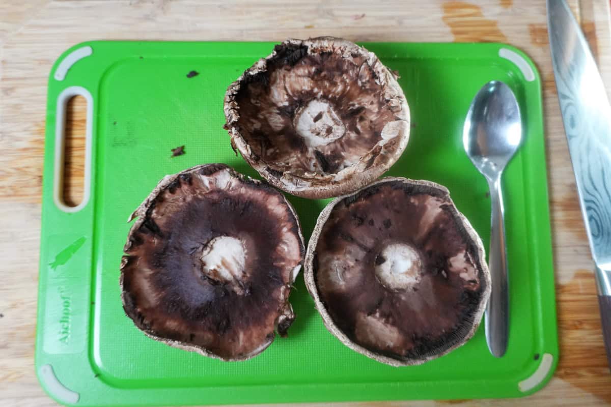 prepped and scrapped portobello mushrooms on a cutting board next to a spoon.