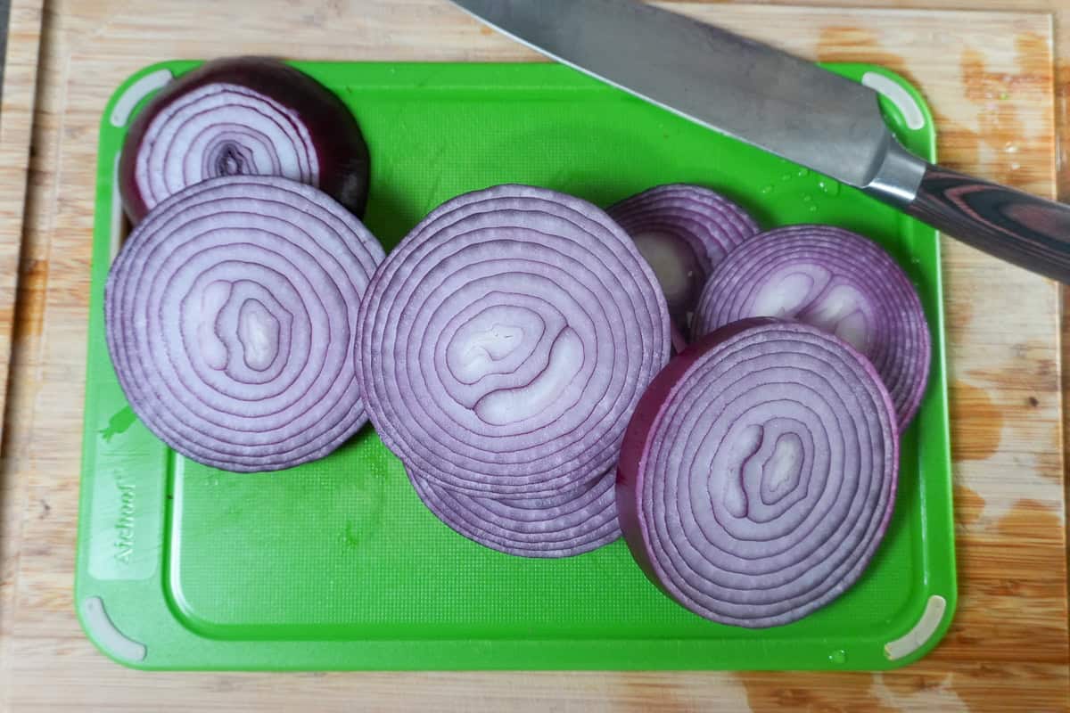 sliced large red onions on a cutting board with a knife.