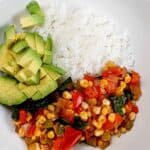 diced avocado added to the wide rim bowl of jasmine rice and vegetable medley.