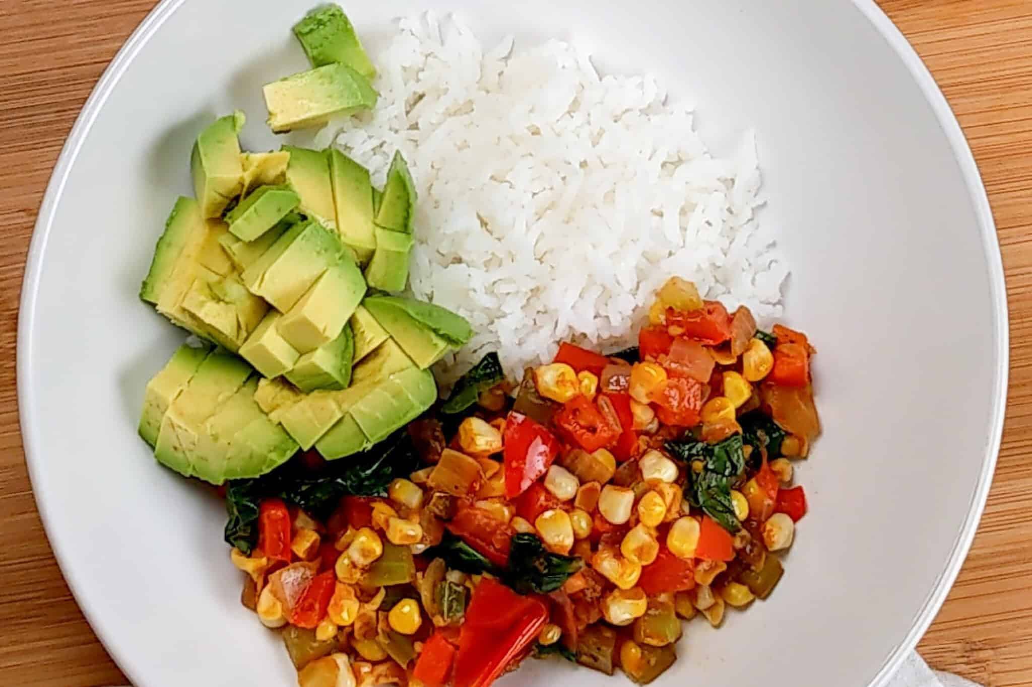 diced avocado added to the wide rim bowl of jasmine rice and vegetable medley.