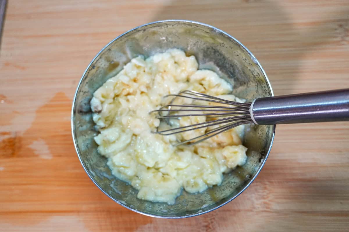 mashed bananas in a small meta bowl with a mini metal whisk.