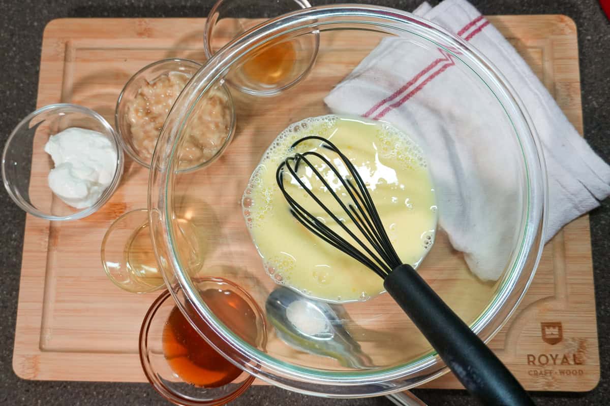 glass mixing bowl with beaten eggs and milk, surrounded by small glass bowls with the rest of the ingredients.