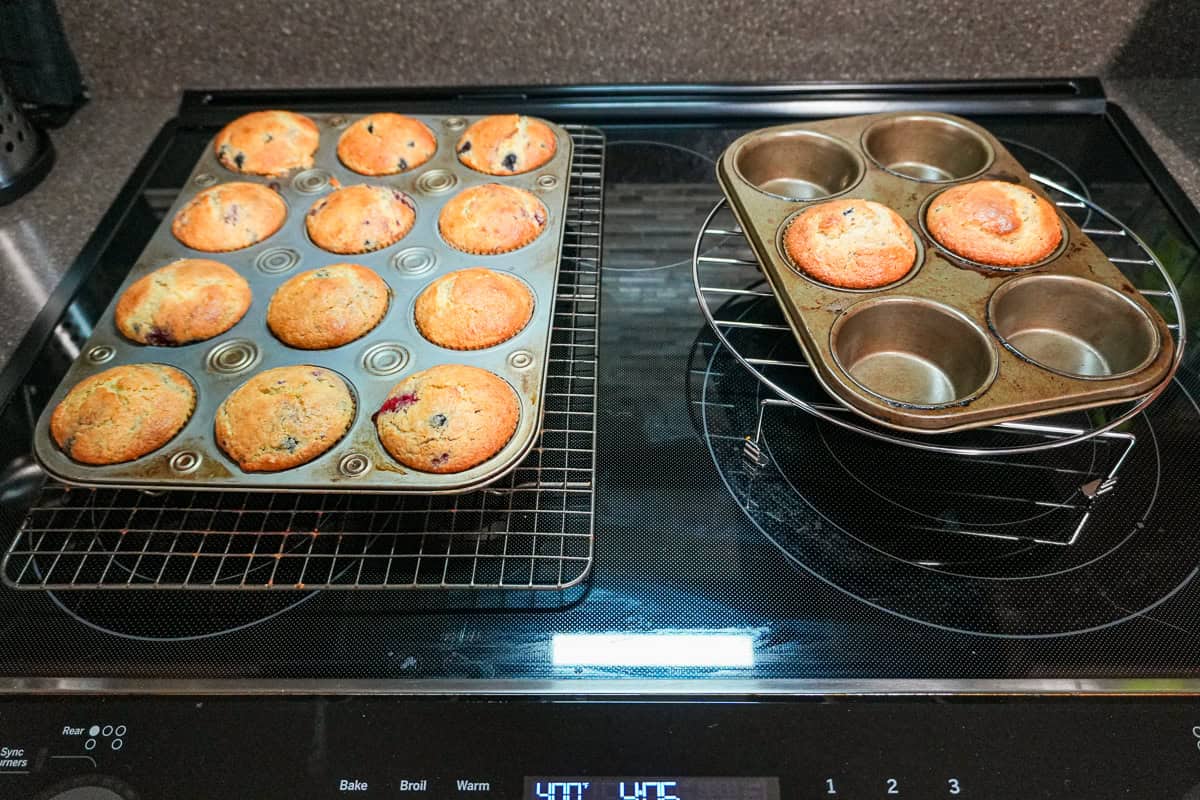 a filled dozen muffin pan and a 6 muffin pan with two baked muffins resting on racks.