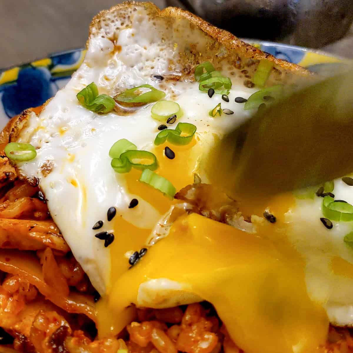 close up of a yolk broken with a spoon from a fried egg on kimchi rice.