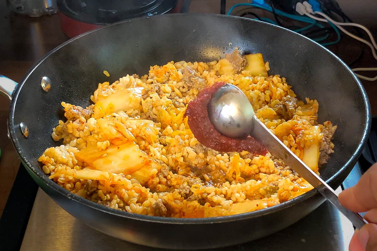 scooped gochujang being added to kimchi rice.