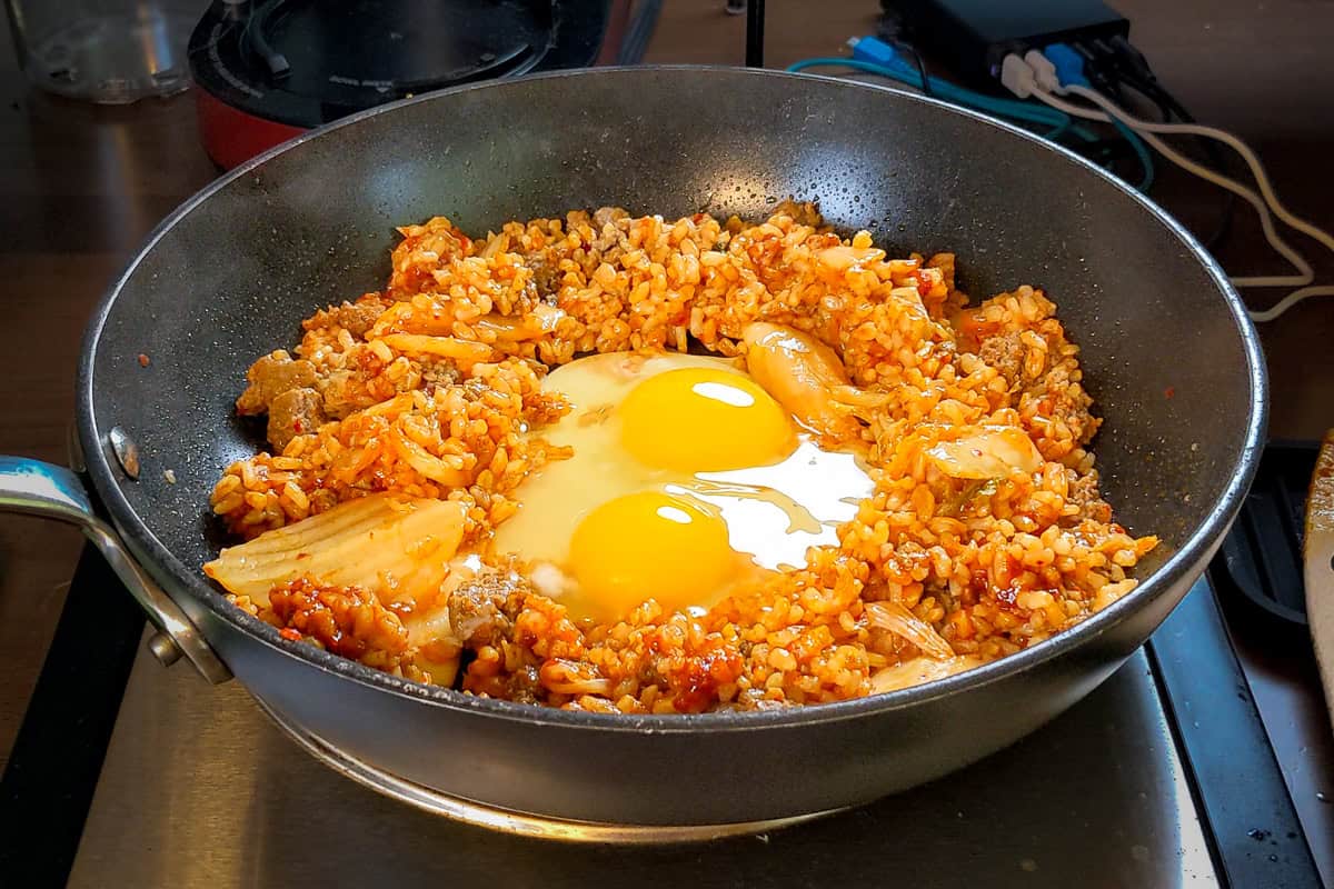 cracked eggs in the center of kimchi fried rice in a saute pan.