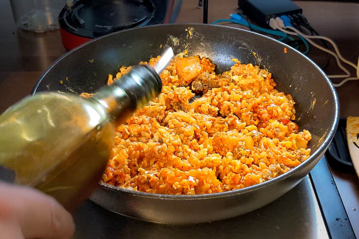 sesame oil being drizzled on fried rice in a saute pan.