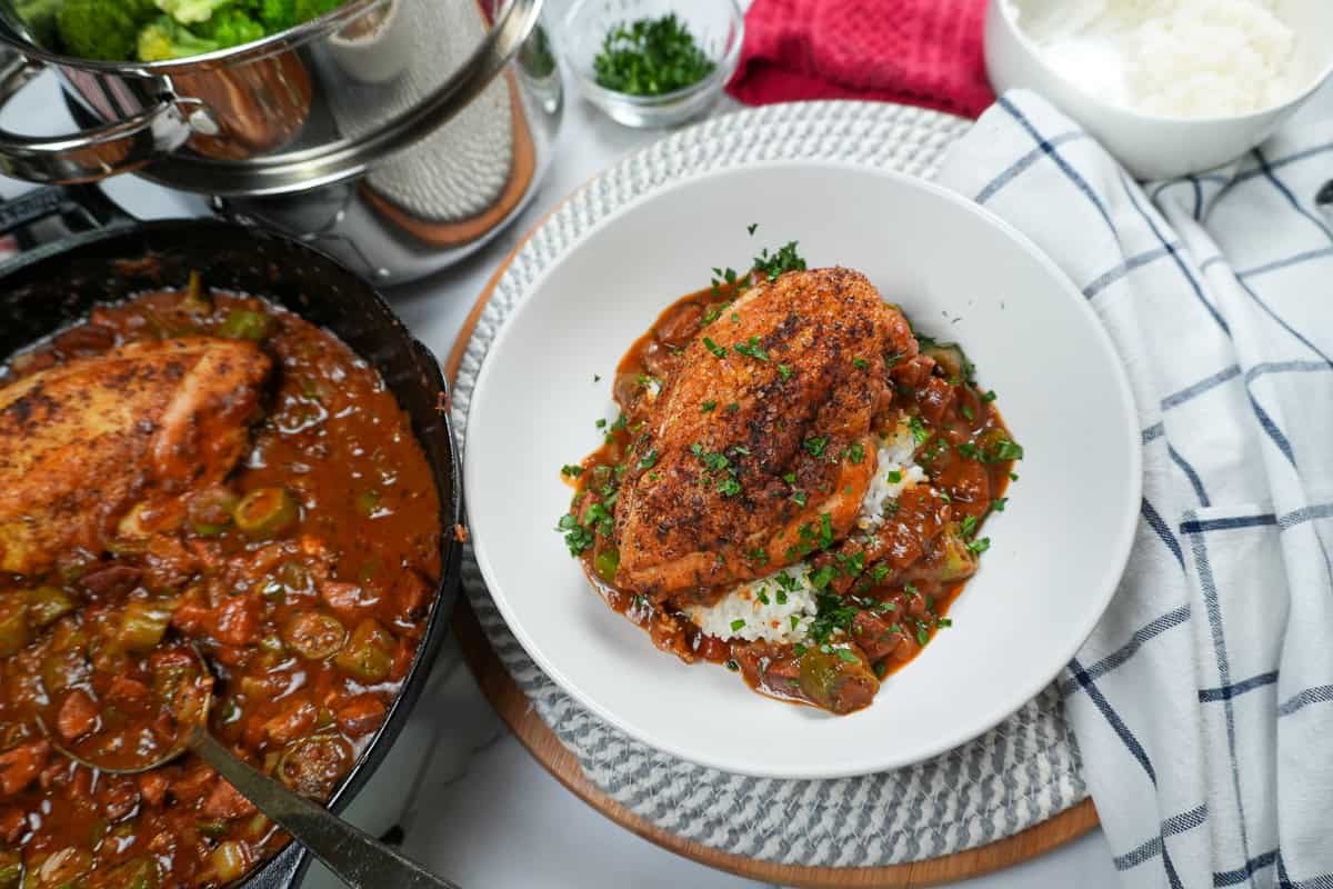 Pan-Roasted Chicken and Andouille Sausage Gumbo in a plate surrounded by more chicken and gumbo in a cast iron skillet and other table settings.