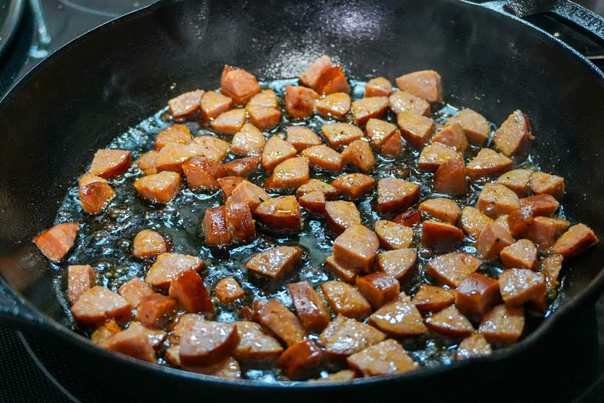 chopped andouille sausage searing in a cast iron skillet.