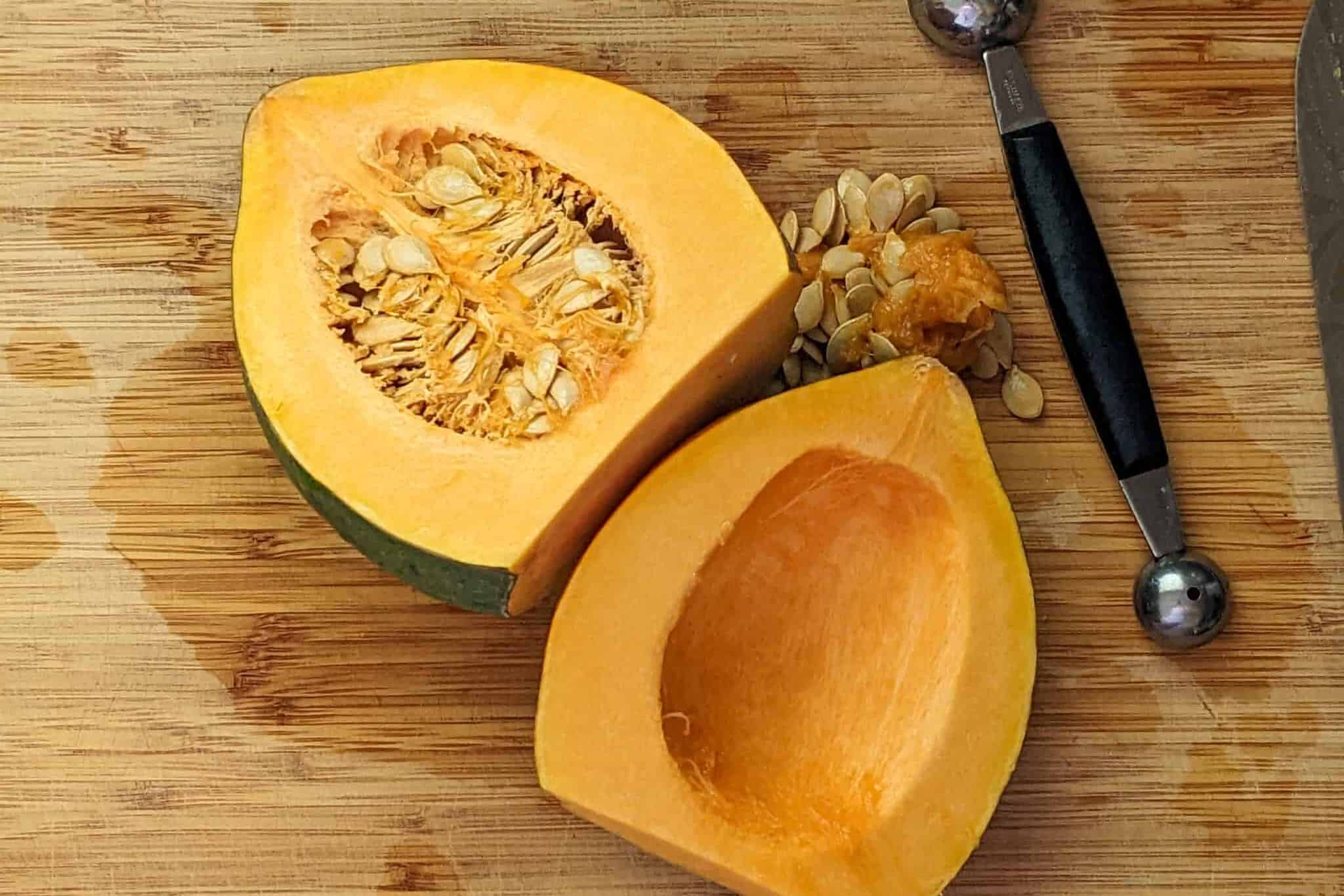 halved acorn squash with one seeded out facing up on a cutting board next to a two-sided melon baller