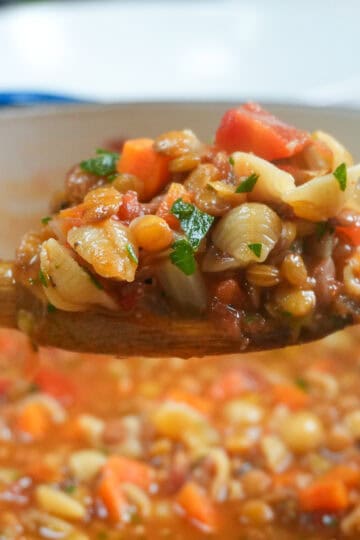 close up of the Pasta and Lentil Soup Recipe on a wooden spoon over a dutch oven fill with the soup.