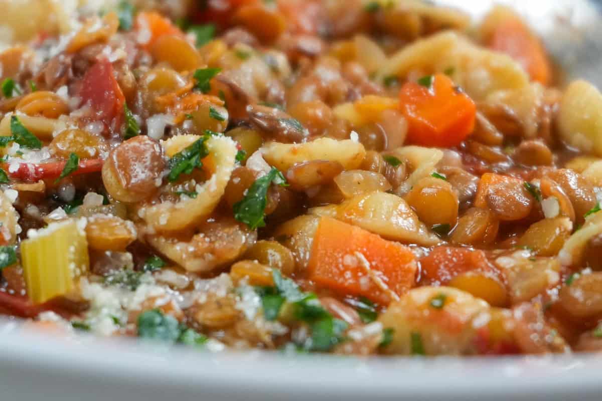 close up of the Pasta and Lentil Soup Recipe in a wide rim bowl topped with chopped parsley and grated cheese.