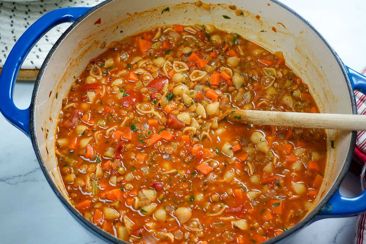 cooked ingredient and the finale of the Pasta and Lentil Soup in a dutch oven with a wooden spoon.