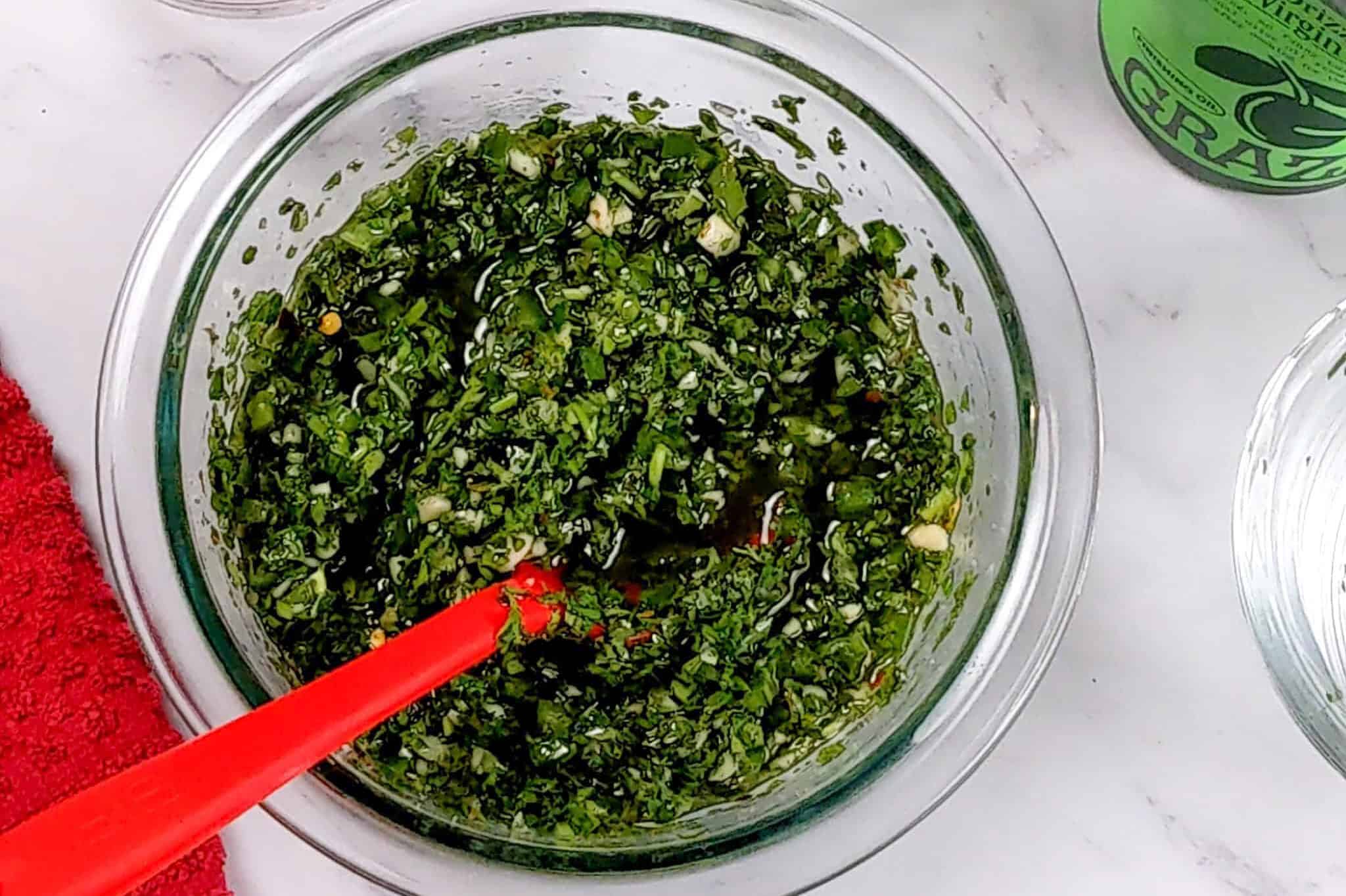 jalapeno chimichurri sauce in a glass mixing bowl with a silicone spoon.