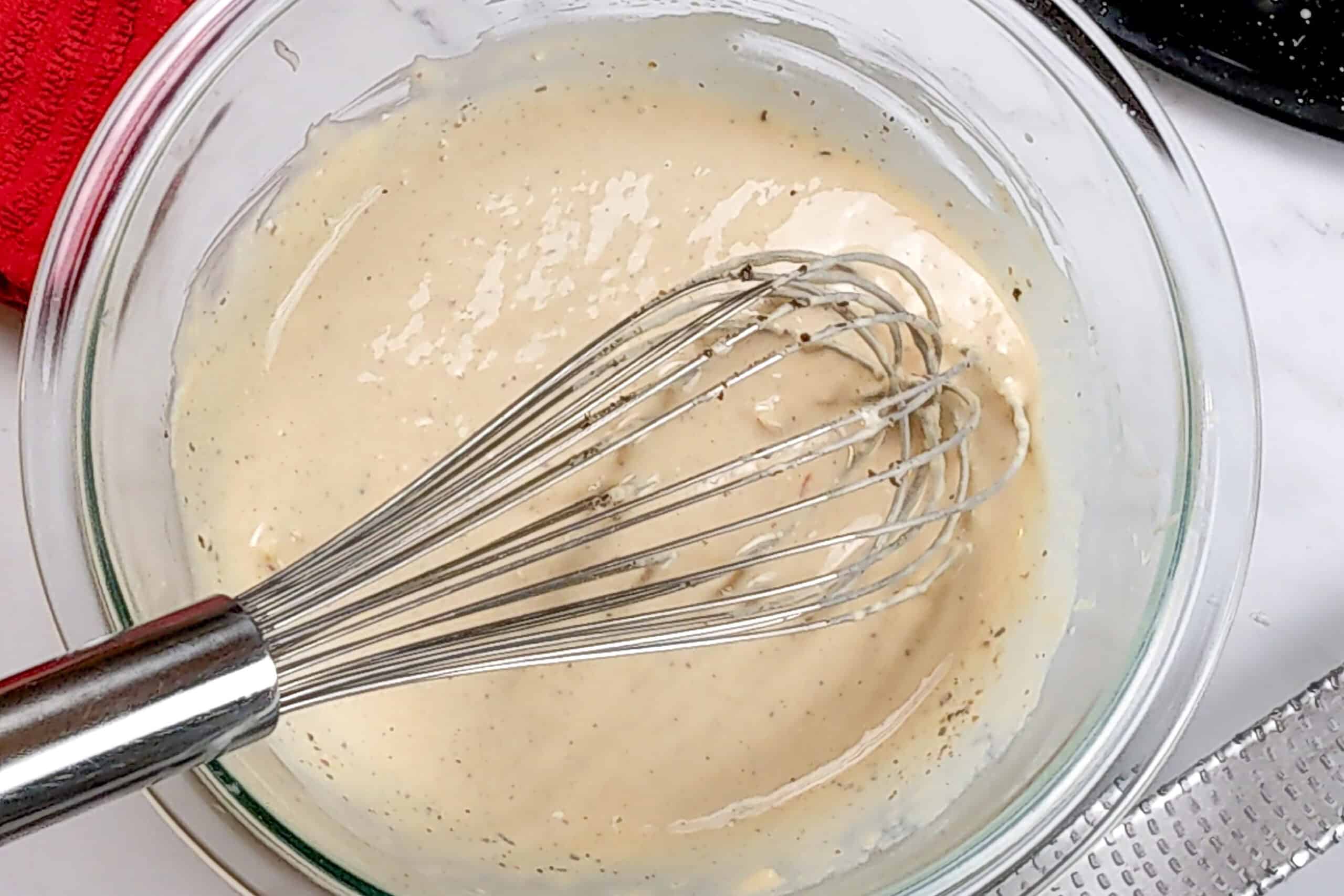 close up of the homemade caesar dressing in a glass bowl with a whisk..