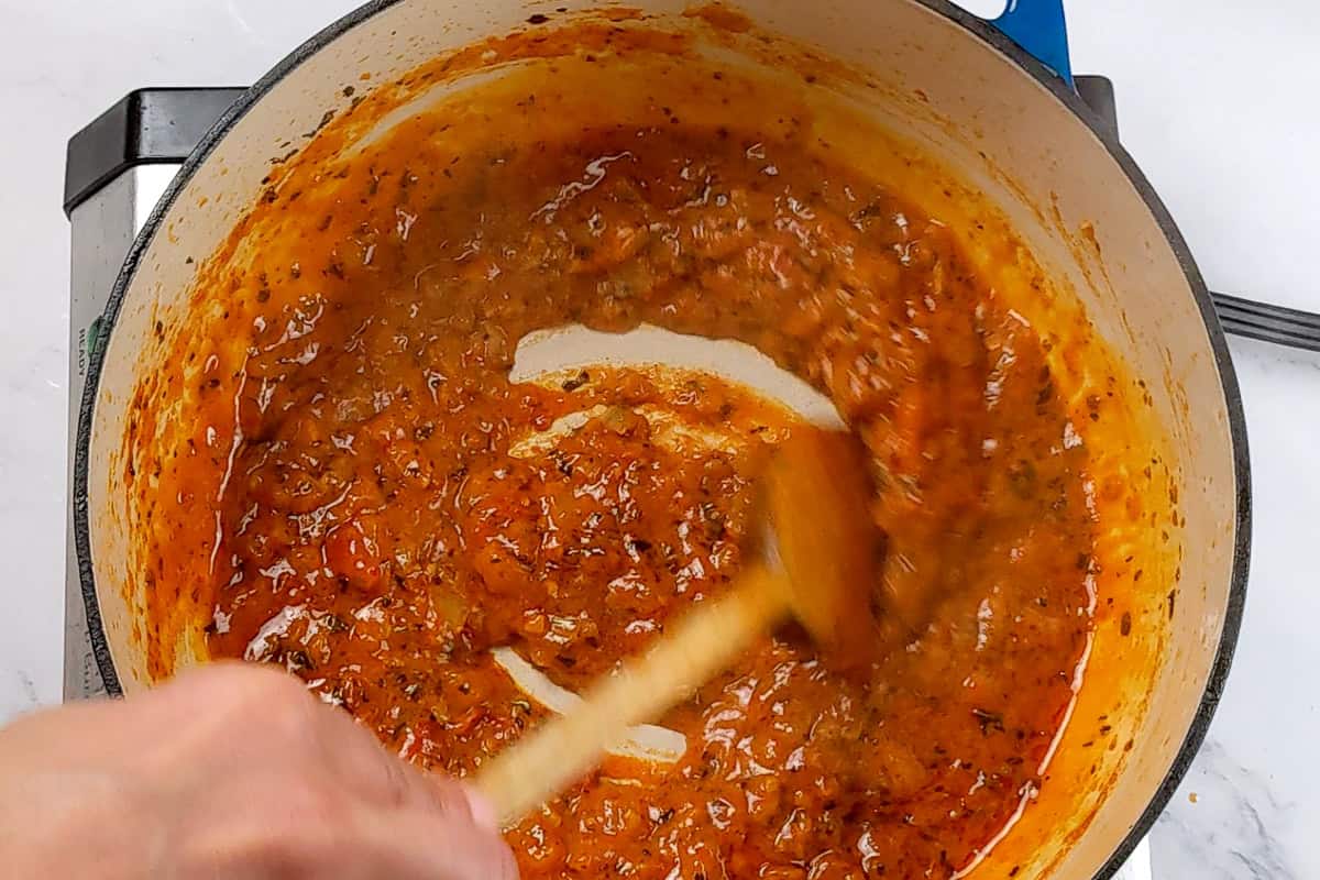 Spicy Garlic Chili Coconut Curry Sauce being stirred in a dutch oven with a wooden spoon.