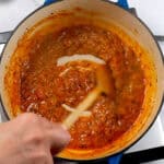 Spicy Garlic Chili Coconut Curry Sauce being stirred in a dutch oven with a wooden spoon.