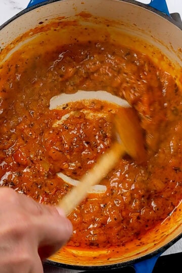 Spicy Garlic Chili Coconut Curry Sauce being stirred in a dutch oven with a wooden spoon.