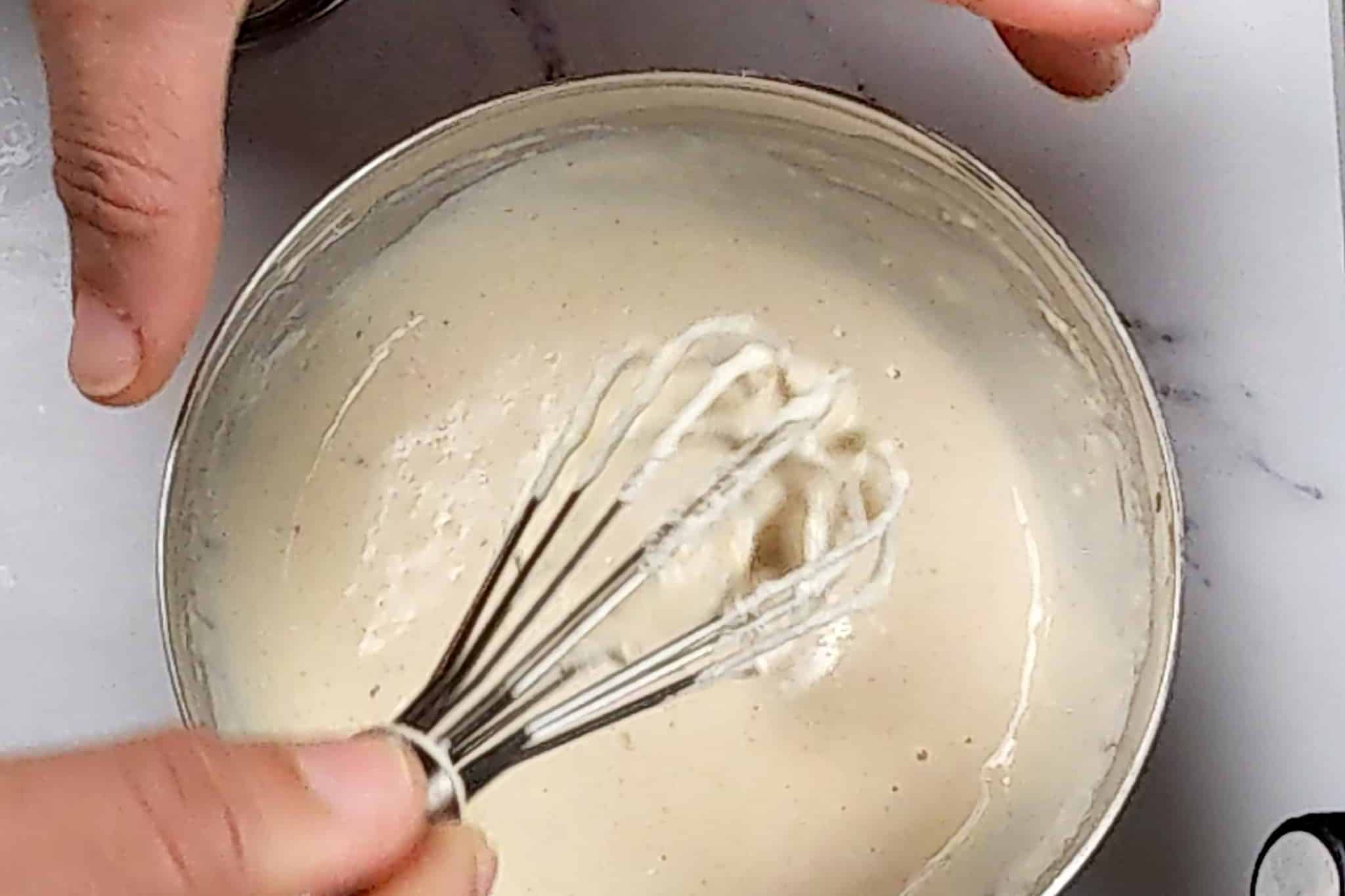 lemon tahini dressing in a small stainless steel mixing bowl with the mini spatula being lifted out.
