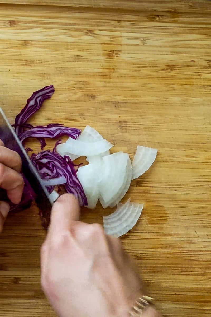 slicing red cabbage and white onions on a wooden cutting board.
