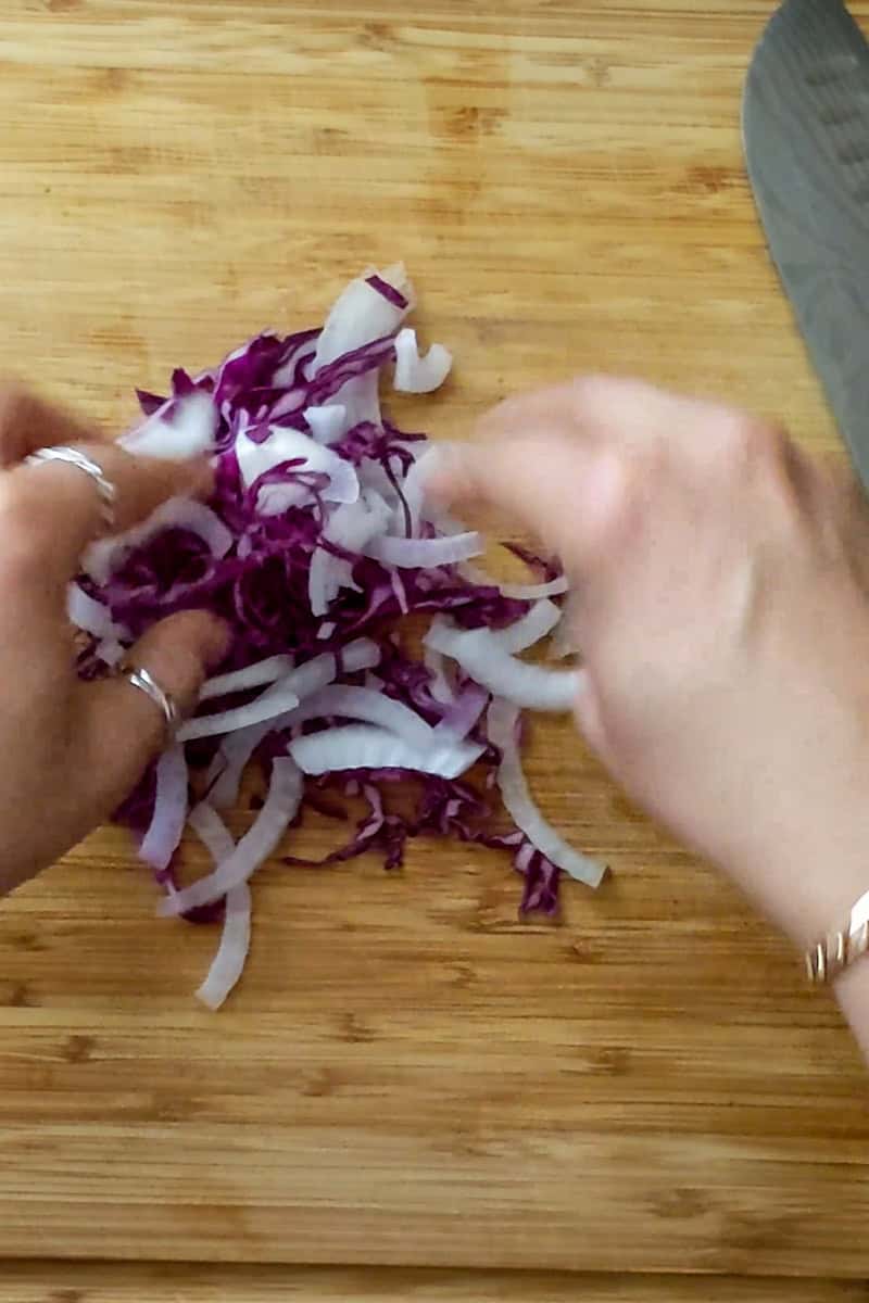 combining sliced cabbage and onion on cutting board.