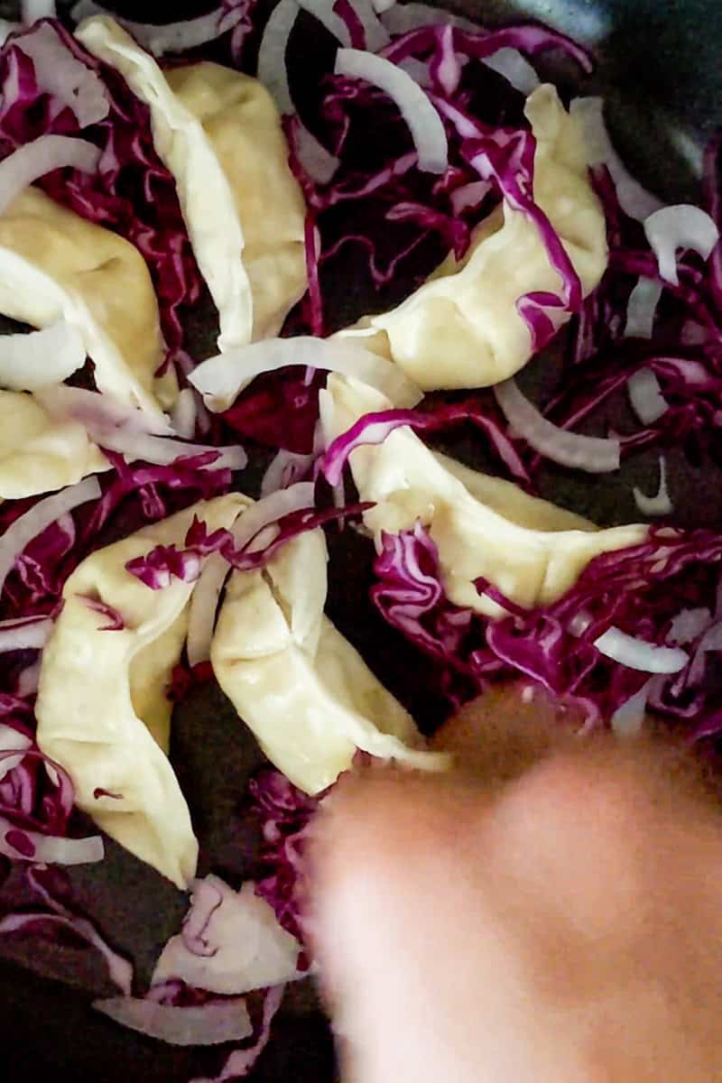 sliced vegetables added to frying pan with dumplings.