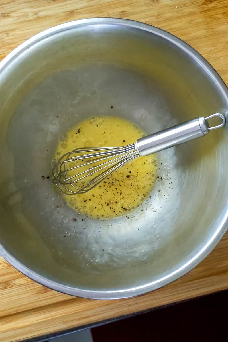metal bowl with beaten seasoned eggs with a whisk laying inside the same bowl.