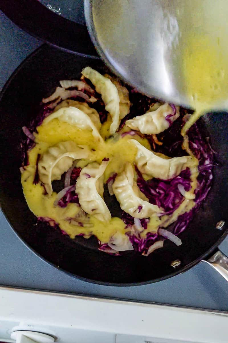 small metal bowl of beaten eggs drizzled around the arranged gyoza.