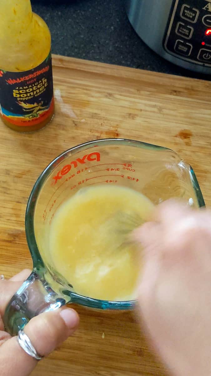 liquid seasoning being whisked with a mini whisk in glass pyrex measuring cup for the jamaican chicken curry stir fry sauce.