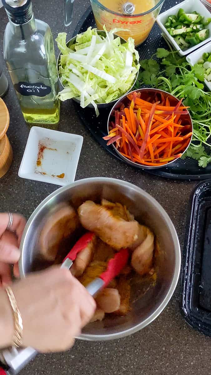 seasoned sliced chicken breast being mixed with a pair of kitchenaid tongs.