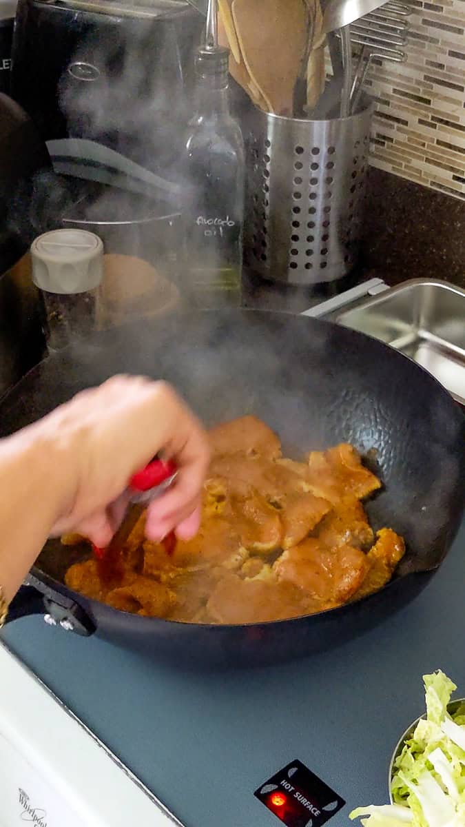 jamaican curry seasoned sliced chicken breast being brown on the stove in a wok.