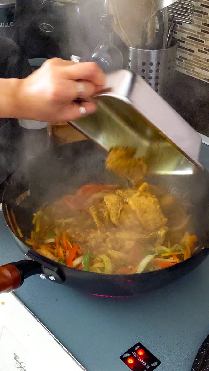 the browned jamaican curry chicken being dropped back into the wok.